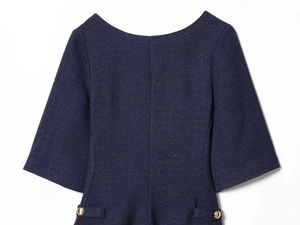 Detail of tweed dress showing texture, gold buttons and decorative pockets on blue fabric