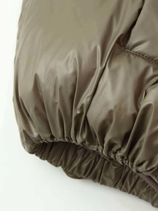 Macro detail of elastic hem on olive green metallic puffer jacket showing high quality stitching