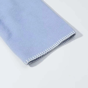 Detailaufnahme von hellblauem Vliesstoff mit präziser weißer Overlock-Stichkante