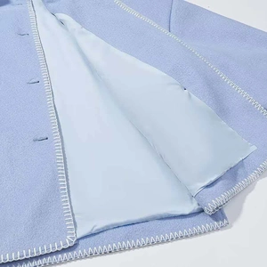 Detail eines hellblauen Wollmantels mit weißen Ziernähten und seidigem Futter