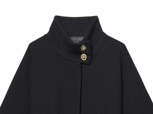 Detalle de chaqueta tipo capa de lana negra con cuello alto y botones dorados