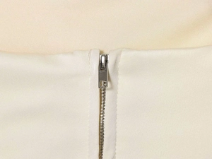 Detailed macro view of the silver metal zipper on cream white woven tube top fabric