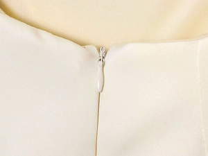 Détail macro de la fermeture éclair invisible sur une robe beige en satin soyeux