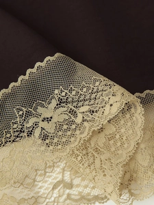 Détail macro de dentelle florale beige délicate sur un tissu satiné sombre