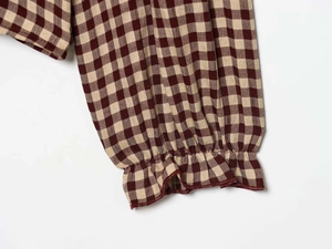 Detail of checkered blouse sleeve with elastic ruffled cuffs in burgundy and beige