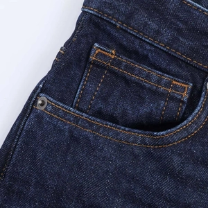 Detailed macro view of dark blue denim fabric with orange contrast stitching and rivets