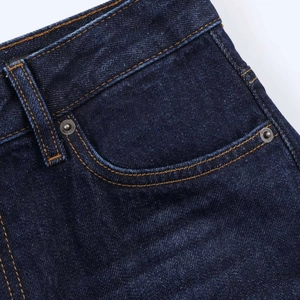 Detailed macro view of dark indigo denim fabric with classic orange contrast stitching