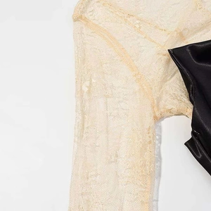 Detail of delicate beige lace stitching on black satin fabric for a slim-fit dress