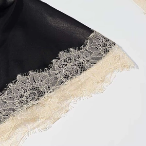 Detail shot of black satin fabric with intricate beige eyelash lace trim on dress