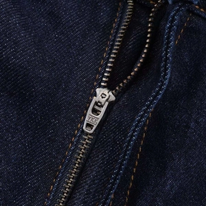 Macro detail of high-quality metal YKK zipper and orange stitching on dark blue denim