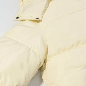 Detailed close-up of light yellow quilted puffer jacket with vintage metal snap button