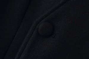 Close-up of premium black wool coat showing fabric texture and matching cloth button