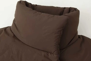 Detail view of the stand-up collar and button closure on this brown padded winter jacket