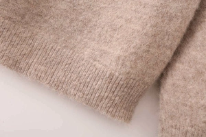 Detailed macro shot of light brown knit fabric with soft wool texture and ribbed hem