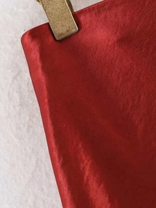Detailed close-up of vibrant red satin fabric texture with elegant gold metal clip detail