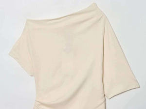 Dettaglio di un top asimmetrico color crema con pieghe eleganti e tessuto dalla trama liscia