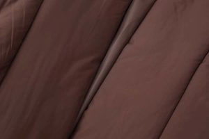 Close-up of chocolate brown quilted fabric showing padded texture and silky sheen