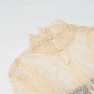 Detail of high neck floral lace blouse with button closure in pale yellow cream fabric