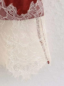 Detailed view of dark red satin fabric with elegant off-white eyelash lace trim at the hem