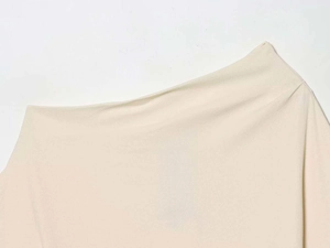 Dettaglio dello scollo asimmetrico color crema con eleganti pieghe in tessuto operato