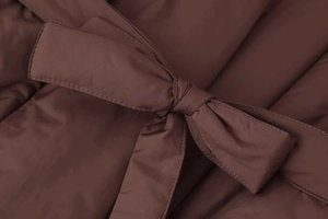 Close-up of dark brown quilted cotton jacket showing waist tie detail and satin finish texture