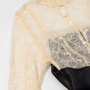 Detailed close-up of beige floral lace bodice and black satin skirt with button accents