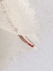 Detail of ivory satin fabric featuring delicate eyelash lace trim and red stitching detail