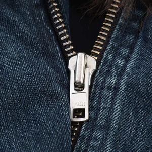 Dettaglio macro della cerniera YKK in metallo su giacca di jeans blu con collo in pelliccia
