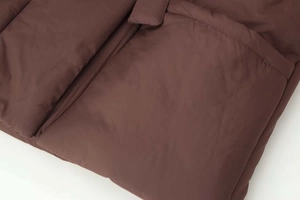 Detailed close-up of dark brown padded jacket featuring horizontal quilting and large pocket