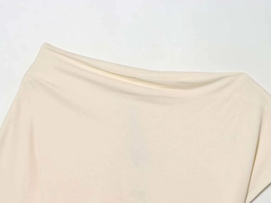 Dettaglio dello scollo asimmetrico e delle pieghe drappeggiate di questo elegante top crema