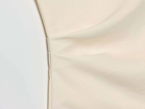 Dettaglio della camicia asimmetrica a pieghe color crema con tessuto effetto raso di lusso