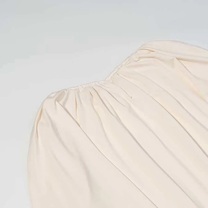 Detail von cremefarbenem Plissee-Stoff mit elastischem gerafftem Ausschnitt am Kleid