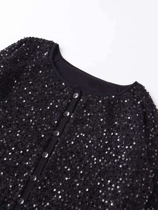 Dettaglio della giacca nera con paillettes, scollo rotondo e bottoni abbinati sul tessuto