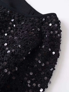 Dettaglio delle paillettes nere sul tessuto in tweed testurizzato di una giacca da donna