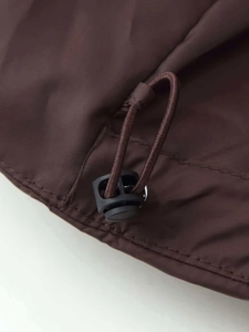 Détail de la veste coupe-vent marron foncé montrant le cordon de serrage et les boucles en plastique
