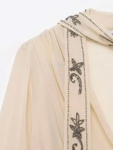 Détail de la broderie de perles et motifs floraux en sequins sur le col d'une blouse crème