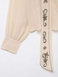 Détail de broderie de perles et motifs d'étoiles sur le poignet du chemisier crème