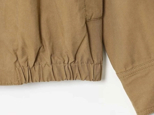 Detail of khaki bomber jacket featuring elastic hem and precise stitching on twill fabric