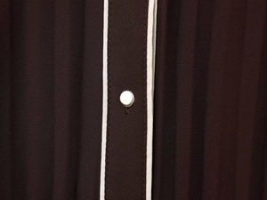 Détail d'une robe midi plissée marron avec bordure blanche et bouton en métal argent