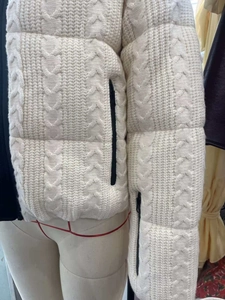 Detail of off-white cable-knit puffer jacket featuring black zipper pockets on mannequin