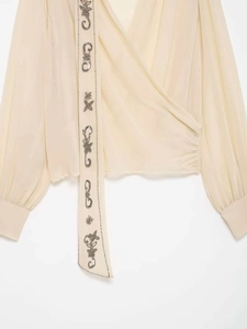 Détails de broderies perlées et motifs floraux sur chemisier beige à col en V