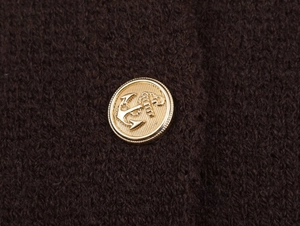 Detail of a golden anchor metal button on dark brown knitted fabric with rich texture