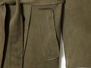 Detail of olive green suede trench coat showing waist belt buckle and side patch pocket