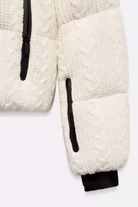 Detail view of white winter puffer jacket with cable knit texture and black zippers