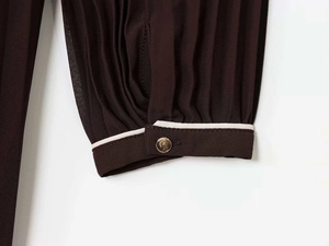 Détail de la manche plissée marron vin avec bordure blanche et bouton doré
