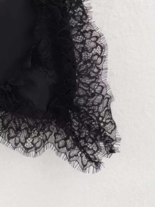Détail de la dentelle florale noire complexe avec bordure de cils sur un haut ample femme