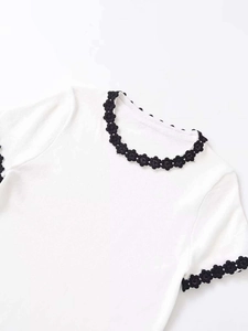 Detailed close-up of white knit top with black 3D flower lace trim on collar and sleeves