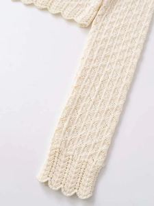 Close-up of cream knit sweater showing hollow geometric patterns and scalloped edges