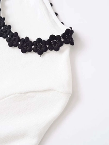 Close-up of black 3D floral lace embroidery on contrast white knit short sleeve top