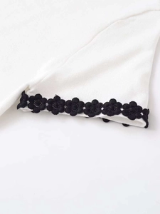 Macro detail of white knit top sleeve with delicate black floral lace trim edge